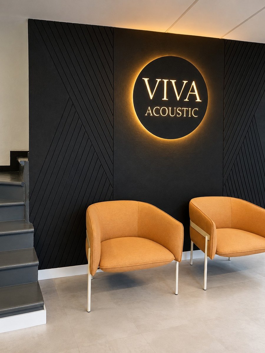 Recepción Oficinas Viva Acoustic Murcia — logo retroiluminado VIVA ACOUSTIC sobre pared de paneles acústicos negros con dos sillones dorados